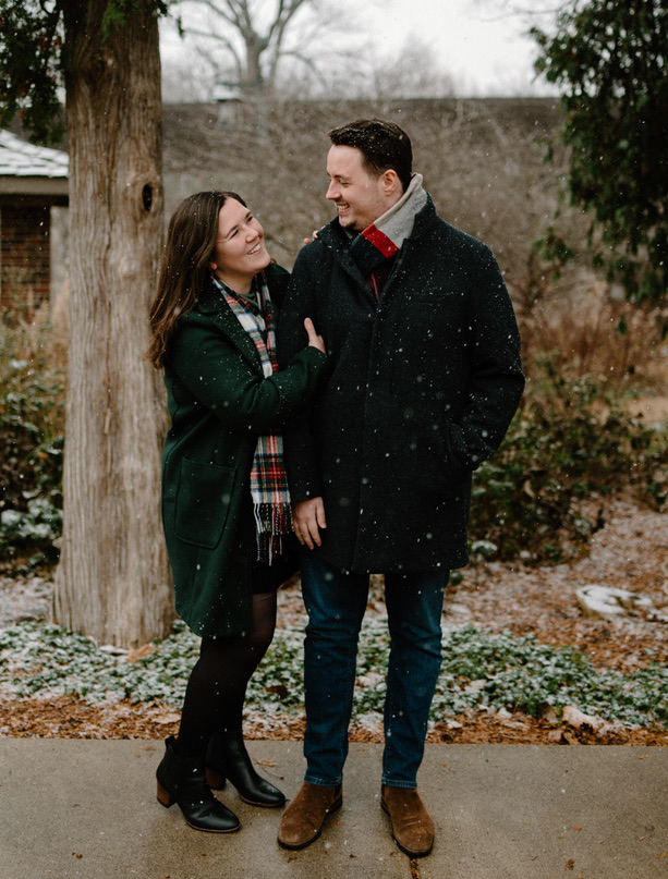 A photo of Tom and Emily looking at each other and smiling in the snow, in Holliday Park in Indianapolis.